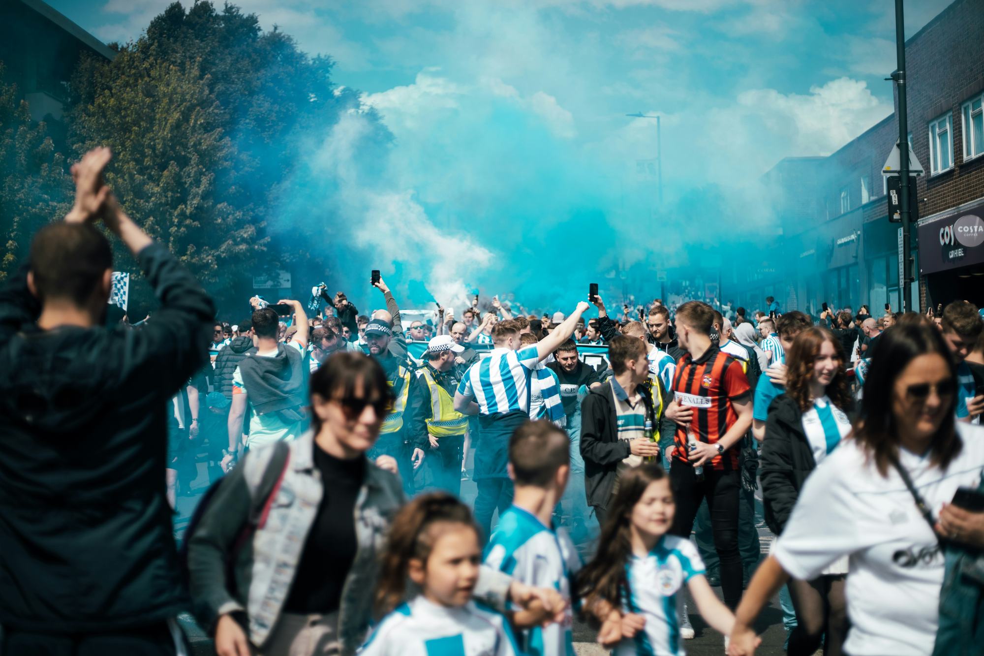Families in club shirts walking to the ground through coloured smoke